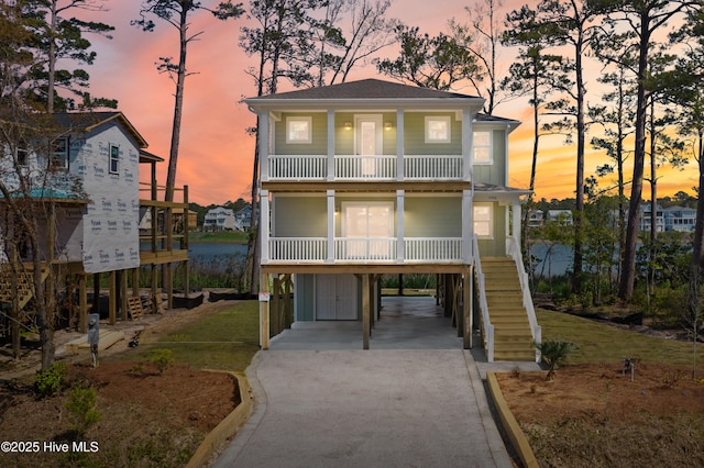 raised beach house featuring a porch, stairway, concrete driveway, a balcony, and a carport