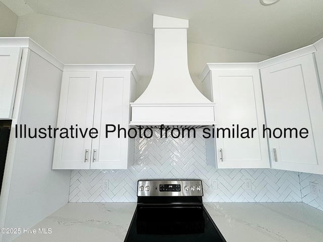 kitchen featuring light stone counters, decorative backsplash, stainless steel range with electric cooktop, white cabinets, and premium range hood