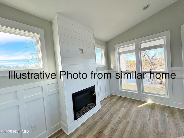 unfurnished living room featuring lofted ceiling, a large fireplace, light wood-style flooring, and a decorative wall