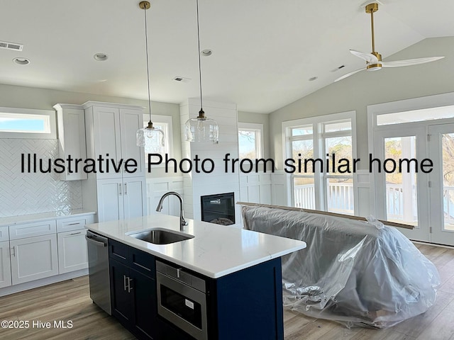 kitchen with stainless steel appliances, a sink, vaulted ceiling, light countertops, and a center island with sink