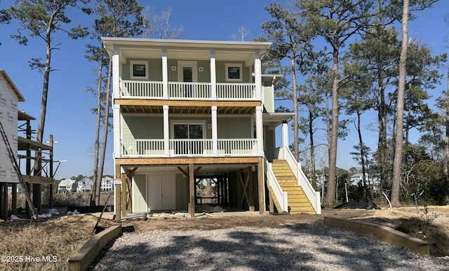 raised beach house with a balcony, stairway, gravel driveway, covered porch, and a carport