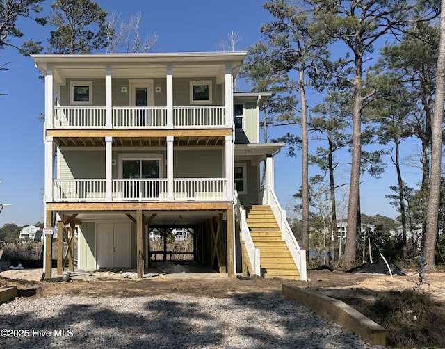 raised beach house featuring dirt driveway, a porch, board and batten siding, a carport, and stairs