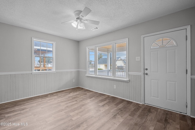 foyer entrance with ceiling fan, a textured ceiling, and light hardwood / wood-style floors