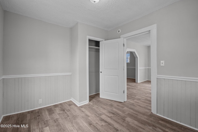 unfurnished bedroom with a textured ceiling, a closet, light hardwood / wood-style flooring, and wood walls