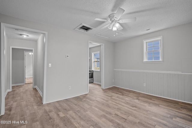 empty room with ceiling fan, wood walls, a textured ceiling, and light hardwood / wood-style flooring