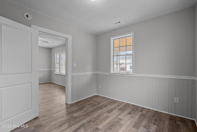 empty room with hardwood / wood-style flooring, a textured ceiling, and a healthy amount of sunlight