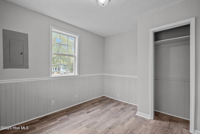 unfurnished bedroom with light hardwood / wood-style floors, a textured ceiling, electric panel, and a closet