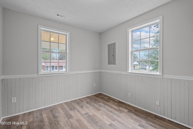 spare room with electric panel, a textured ceiling, and light hardwood / wood-style flooring