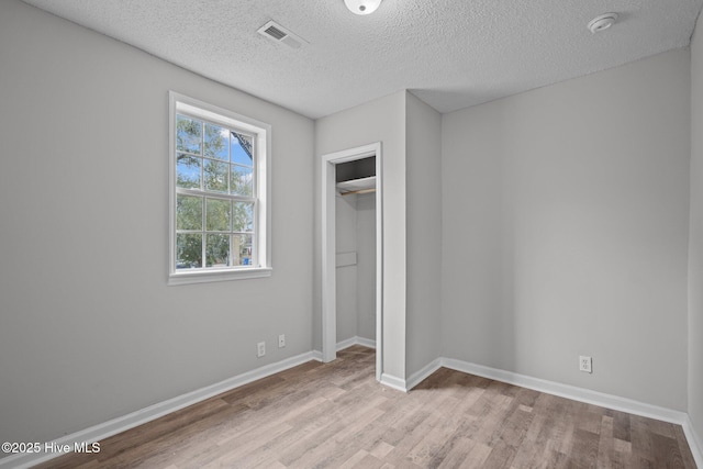 unfurnished bedroom featuring a textured ceiling, a closet, and light hardwood / wood-style floors