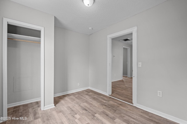 unfurnished bedroom featuring a textured ceiling, a closet, and light hardwood / wood-style flooring