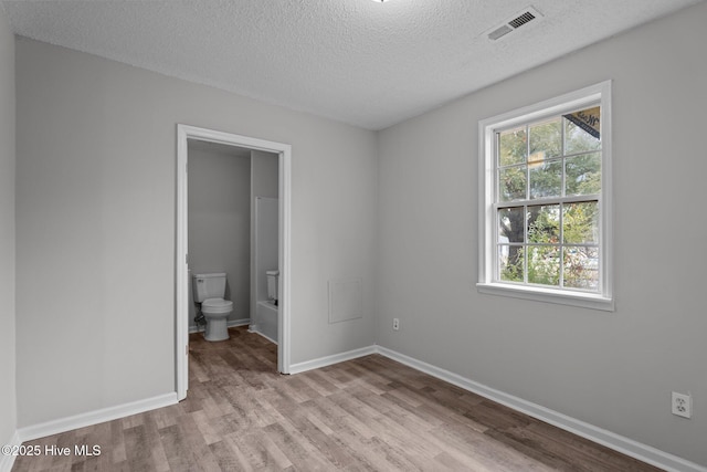 unfurnished bedroom with connected bathroom, light hardwood / wood-style flooring, multiple windows, and a textured ceiling