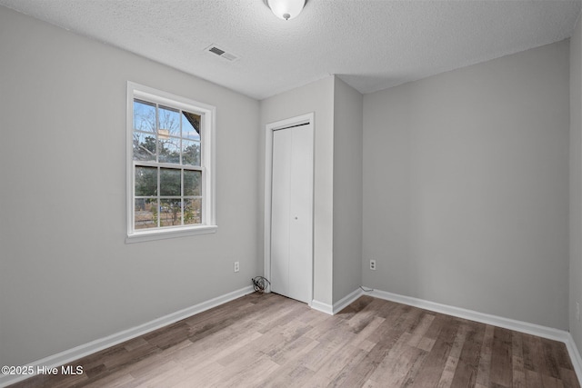 unfurnished bedroom featuring light hardwood / wood-style floors, a textured ceiling, and a closet