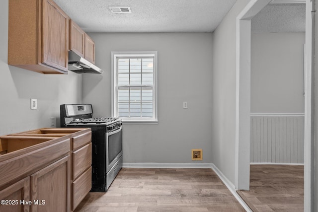 kitchen featuring light hardwood / wood-style floors, a textured ceiling, and stainless steel gas range oven