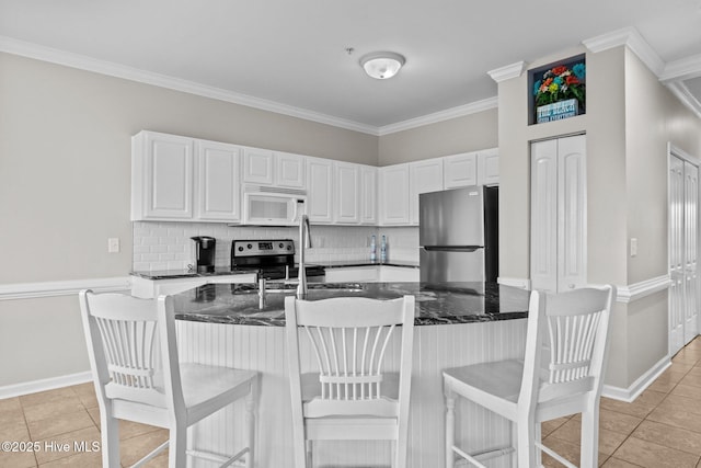 kitchen with white cabinetry, crown molding, dark stone countertops, light tile patterned floors, and appliances with stainless steel finishes