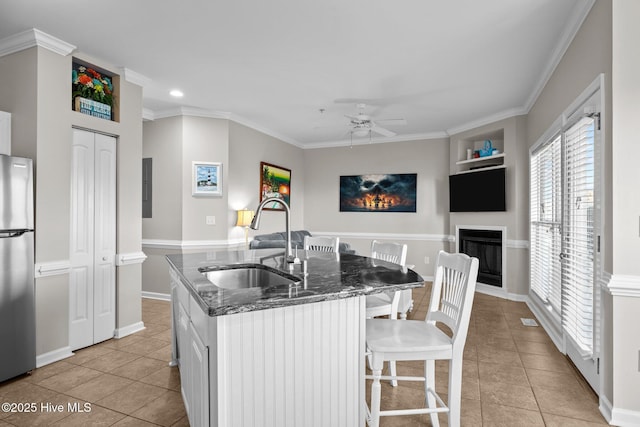 kitchen featuring sink, light tile patterned floors, stainless steel refrigerator, a kitchen island with sink, and white cabinets