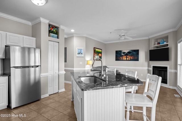 kitchen with sink, light tile patterned floors, stainless steel fridge, white cabinets, and a center island with sink