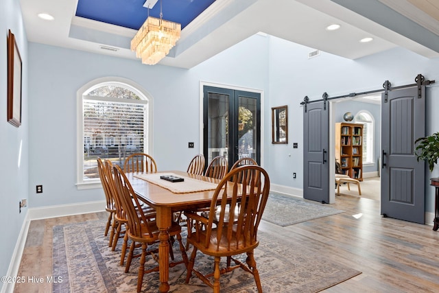 dining room featuring hardwood / wood-style floors, ornamental molding, a raised ceiling, french doors, and a barn door