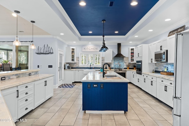 kitchen with sink, decorative light fixtures, a raised ceiling, a kitchen island with sink, and wall chimney range hood