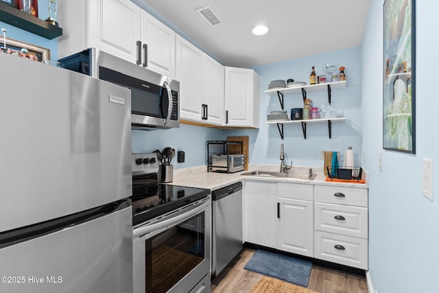 kitchen with appliances with stainless steel finishes, sink, white cabinets, and light hardwood / wood-style floors