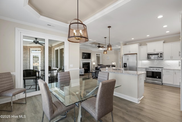 dining space featuring hardwood / wood-style floors, a tray ceiling, ornamental molding, ceiling fan with notable chandelier, and sink