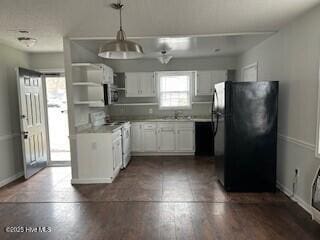 kitchen with black fridge, white cabinetry, and pendant lighting