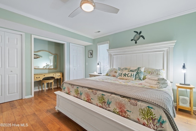 bedroom with crown molding, ceiling fan, hardwood / wood-style floors, and two closets