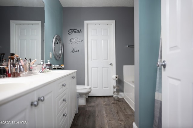 full bathroom featuring double vanity, toilet, wood finished floors, a garden tub, and a sink