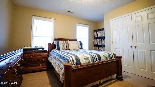 carpeted bedroom featuring a textured ceiling, visible vents, and a closet