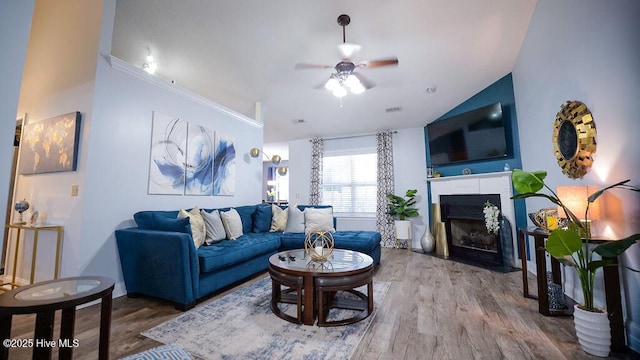 living area with lofted ceiling, a fireplace with flush hearth, ceiling fan, and wood finished floors