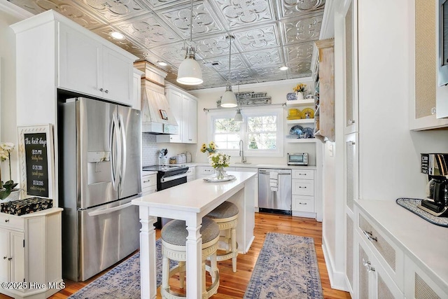 kitchen featuring sink, white cabinetry, hanging light fixtures, custom range hood, and stainless steel appliances