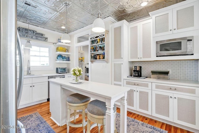 kitchen with sink, hanging light fixtures, stainless steel appliances, white cabinets, and light wood-type flooring