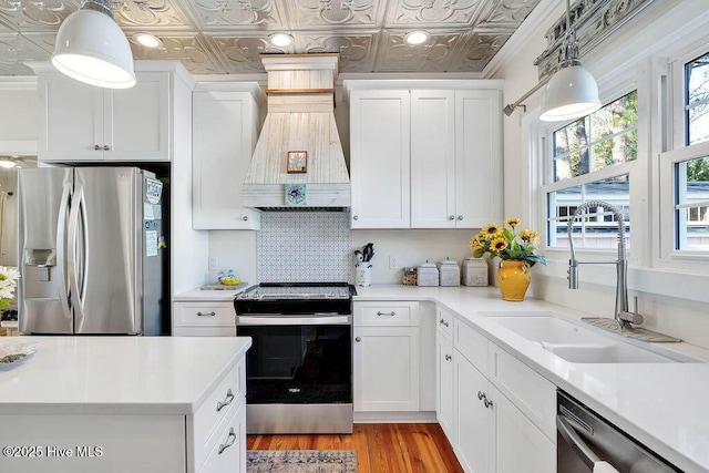 kitchen featuring premium range hood, sink, hanging light fixtures, appliances with stainless steel finishes, and white cabinets