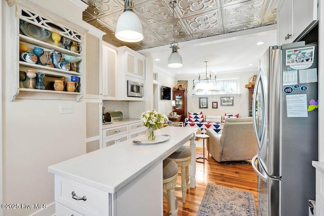 kitchen featuring a breakfast bar area, tasteful backsplash, stainless steel appliances, light hardwood / wood-style floors, and white cabinets