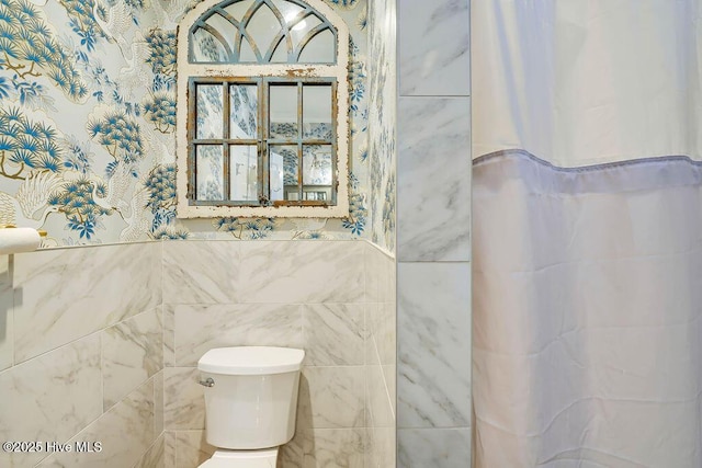 bathroom featuring a shower with curtain, toilet, and tile walls