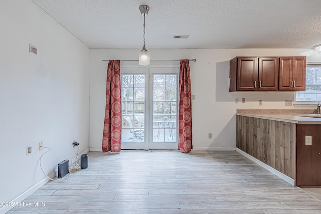 kitchen featuring decorative light fixtures, sink, a textured ceiling, and light wood-type flooring