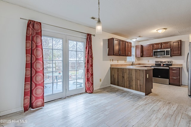 kitchen with kitchen peninsula, stainless steel appliances, light wood-type flooring, hanging light fixtures, and a textured ceiling