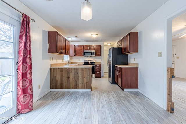 kitchen featuring pendant lighting, light hardwood / wood-style floors, kitchen peninsula, sink, and stainless steel appliances