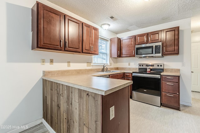 kitchen featuring a textured ceiling, stainless steel appliances, kitchen peninsula, and sink