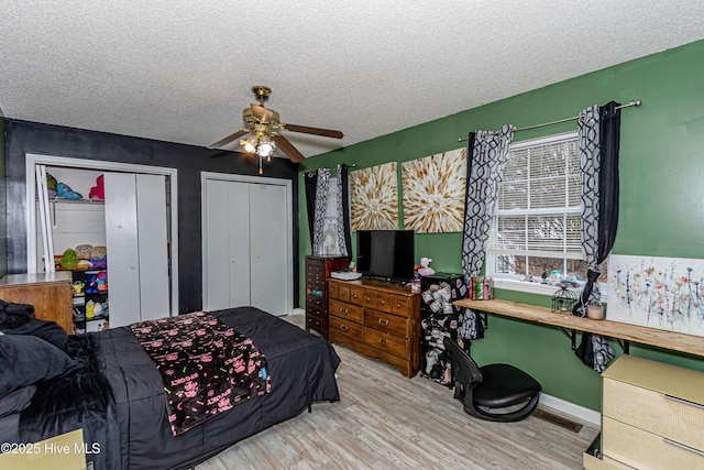 bedroom featuring ceiling fan, light wood-type flooring, multiple closets, and a textured ceiling