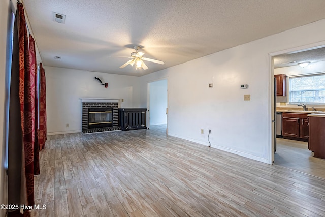 unfurnished living room with ceiling fan, light wood-type flooring, a brick fireplace, and a textured ceiling