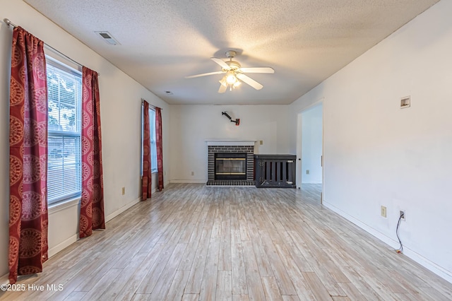 unfurnished living room featuring light wood-type flooring, ceiling fan, a textured ceiling, and a fireplace