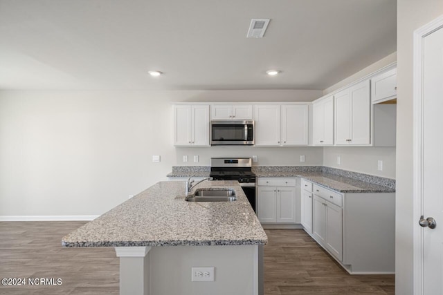 kitchen featuring a center island with sink, white cabinetry, hardwood / wood-style flooring, stainless steel appliances, and light stone counters