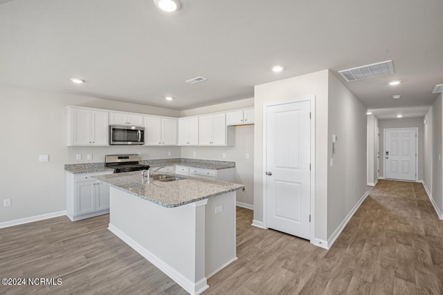 kitchen with light stone countertops, white cabinetry, stainless steel appliances, an island with sink, and sink