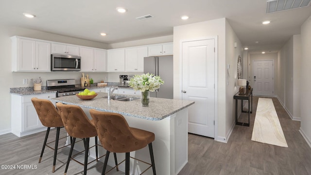 kitchen with sink, a kitchen island with sink, light stone countertops, appliances with stainless steel finishes, and white cabinets