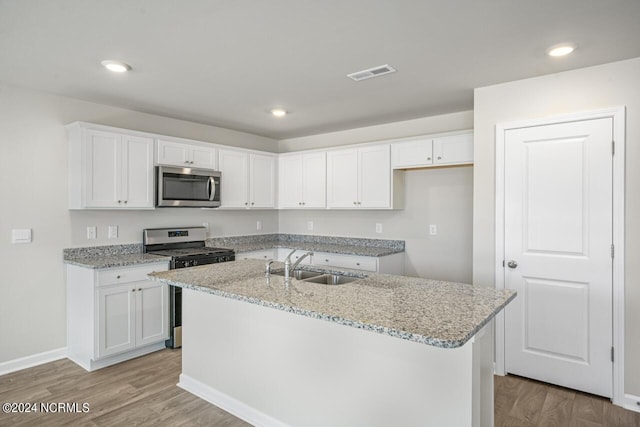 kitchen with a center island with sink, sink, white cabinetry, light wood-type flooring, and stainless steel appliances