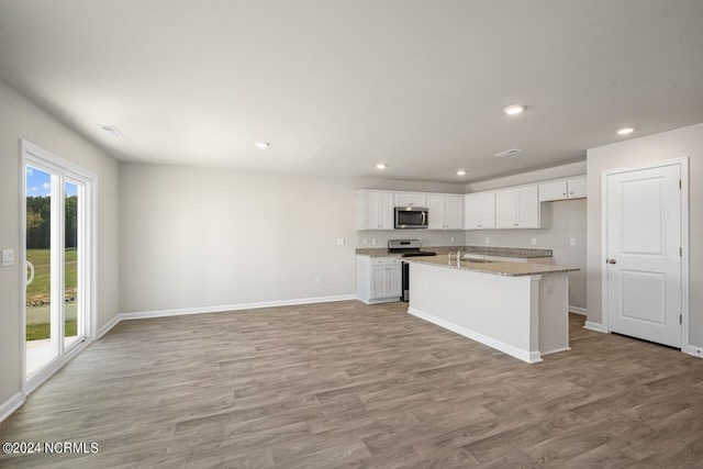 kitchen with light hardwood / wood-style floors, white cabinetry, a kitchen island with sink, stainless steel appliances, and light stone counters