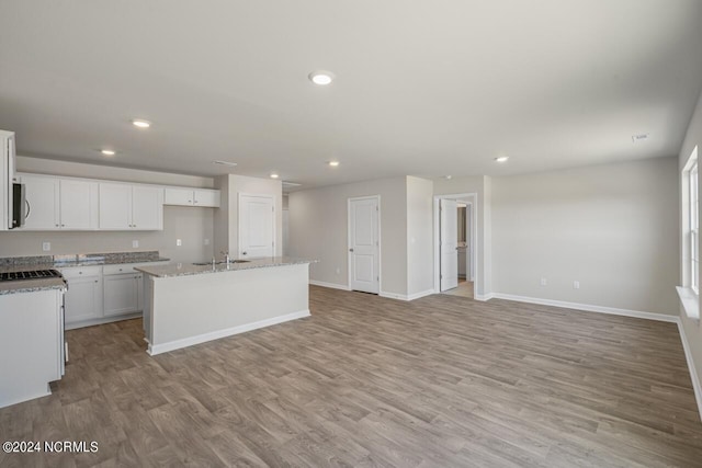 kitchen with light stone counters, white cabinetry, a center island with sink, and light wood-type flooring