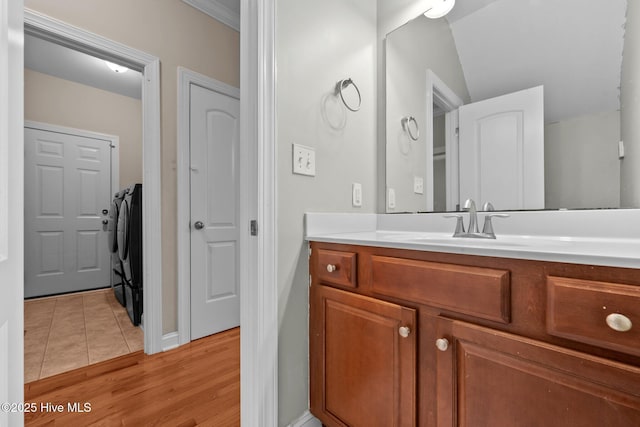 bathroom featuring washing machine and dryer, wood-type flooring, ornamental molding, and vanity