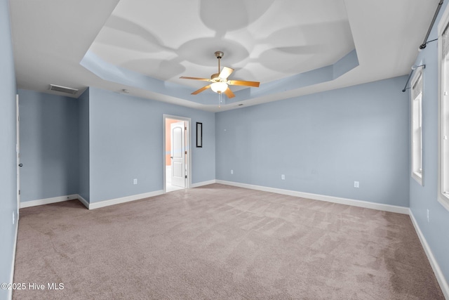 empty room with ceiling fan, light colored carpet, and a tray ceiling