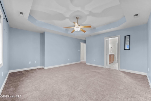 spare room featuring a raised ceiling and light colored carpet